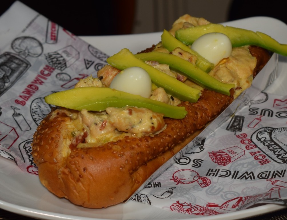 Perro Mexicano (Pan brioche, salchicha, Tocineta humada, Pollo en salsa de quesos, Aguacate, Papitas, Cebolla picada)